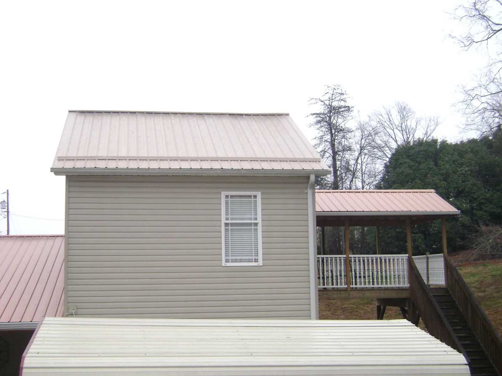 Tan metal roofs on a two story addition and attached porch, from a Roof Replacement job in Crown Point